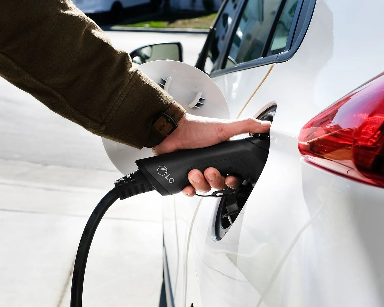 Close-up of a hand plugging an electric vehicle charger into a sleek white car, highlighting eco-friendly transportation.