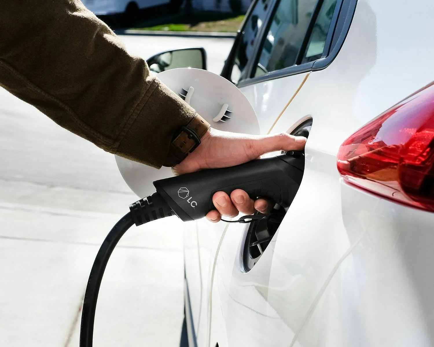 Close-up of an electric vehicle being charged with a sleek, modern charging cable in bright sunlight.