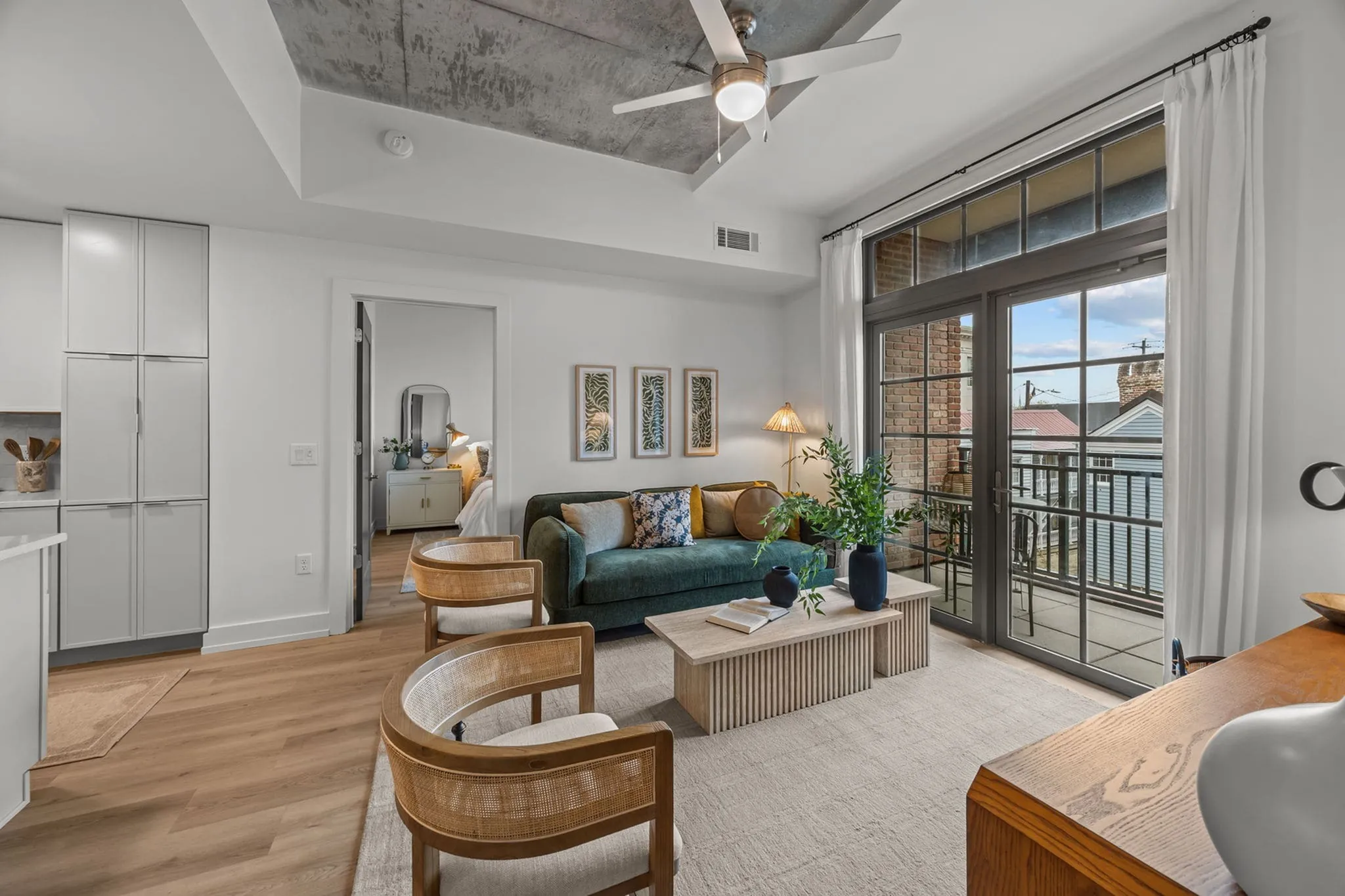 Sleek living room with modern decor, featuring a plush green sofa, wooden accents, and large windows opening to a charming balcony.