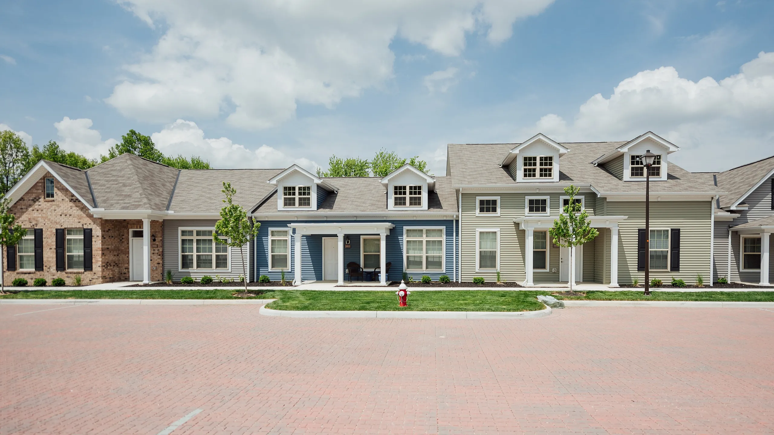 Charming row of modern townhouses with dormer windows and manicured lawns under a bright sky.