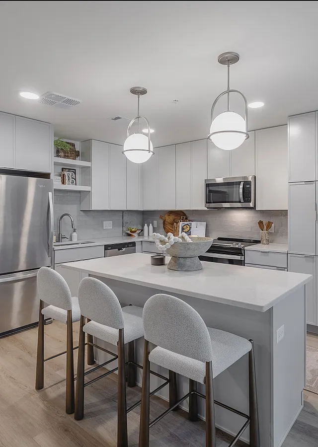 Modern kitchen with sleek white cabinets, spacious island seating, and stainless steel appliances under elegant hanging lights.
