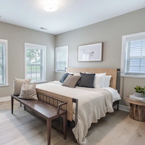 Bright and inviting bedroom with stylish decor, featuring a cozy bed, natural light from multiple windows, and modern furnishings.