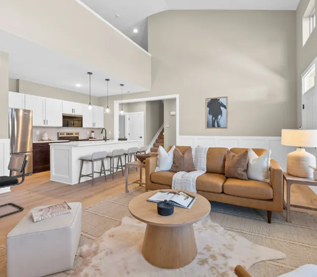 Elegant open-concept living space featuring a cozy tan sofa, modern kitchen with island seating, and stylish decor accents.