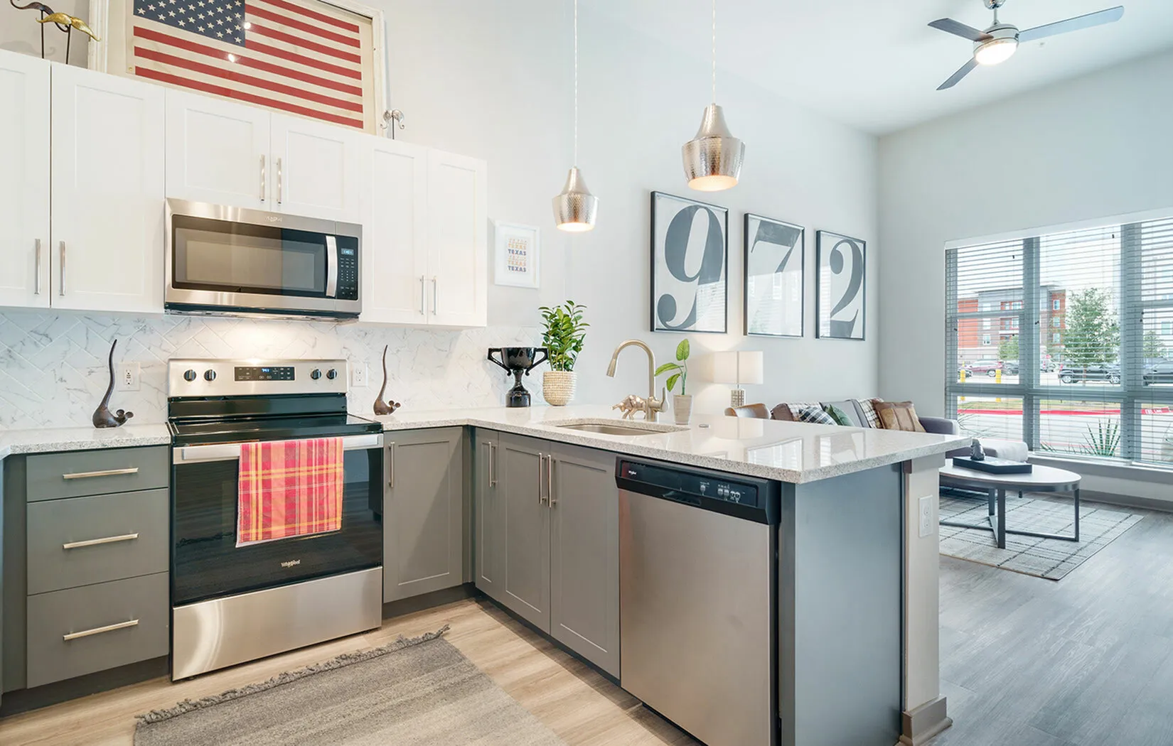 Modern kitchen with sleek stainless steel appliances, elegant pendant lighting, and a spacious island seamlessly flowing into a bright living room with large windows.