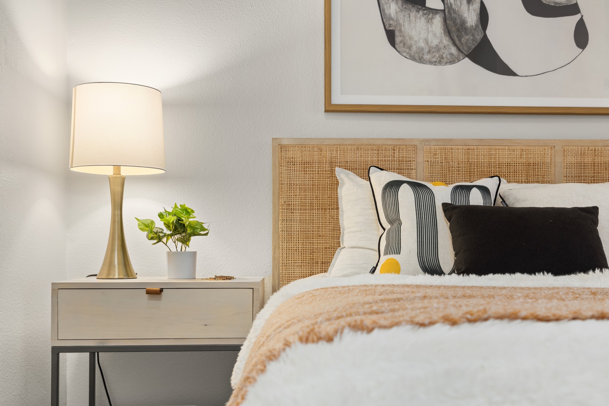 wicker bed headboard with nightstand and lamp. artwork frame on wall.