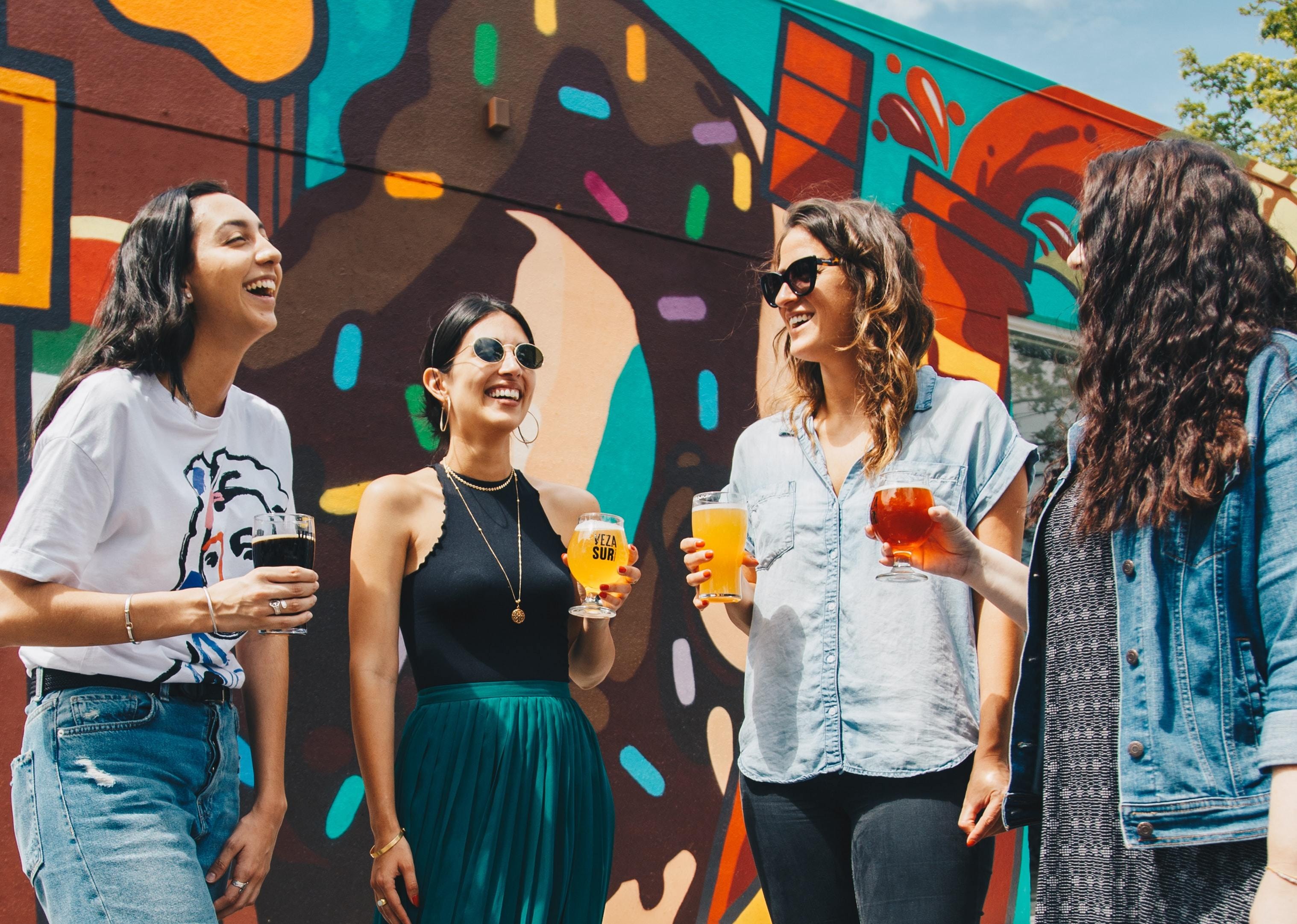 friends enjoying drinks outside in front of a painted mural