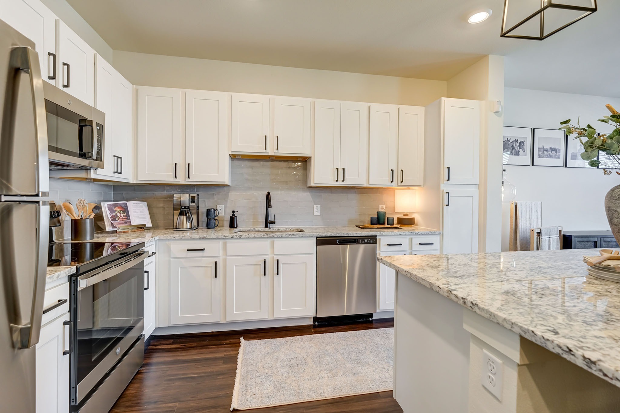 Kitchen with stainless steel appliances, quartz countertops, tiled backsplash, white cabinetry, hardwood-style flooring, and black fixtures