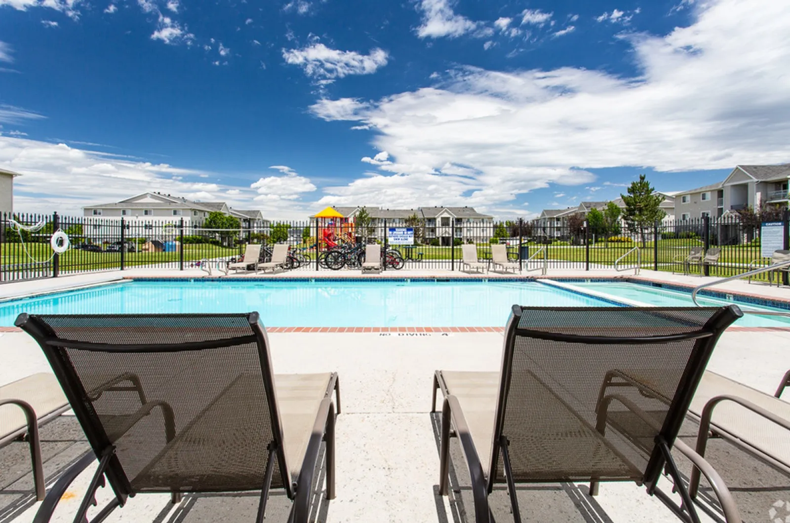 Sunny day, pool, bike rack, and playground in background.