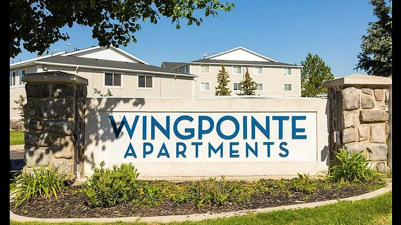 Entrance sign for Wingpointe Apartments with modern residential buildings and landscaped greenery in the background.