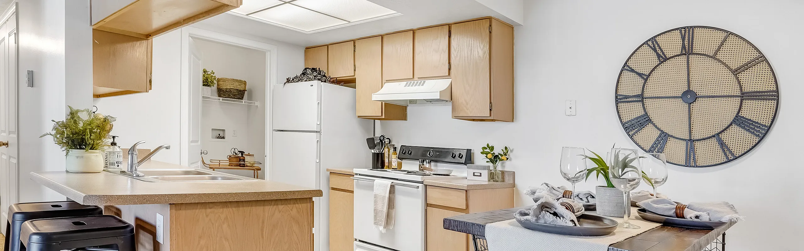 Modern kitchen with wooden cabinets, a white fridge and stove, and a stylish dining table for two.