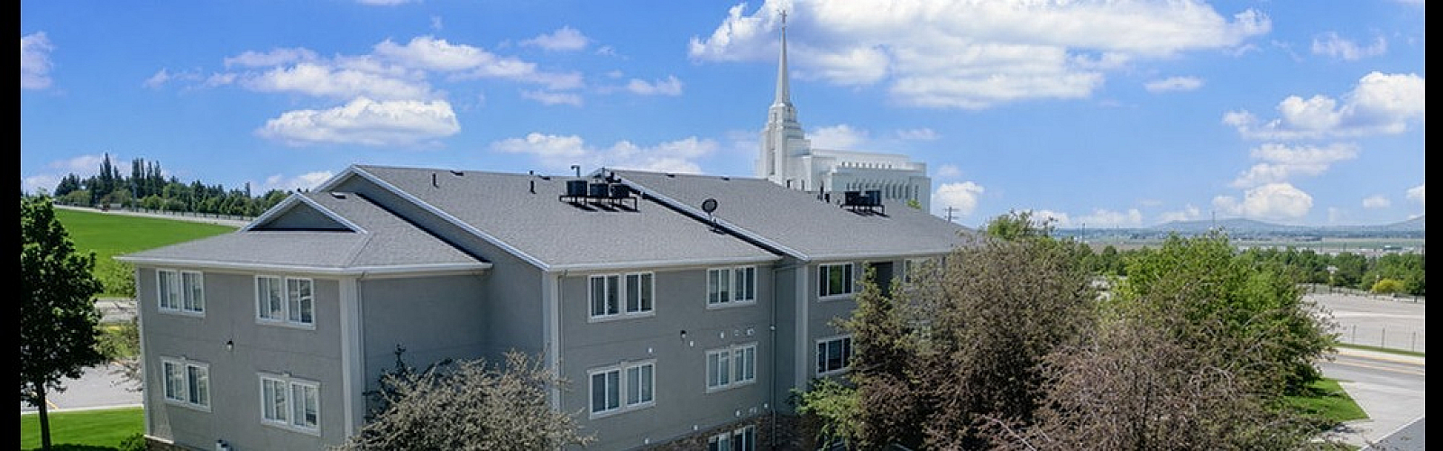 Elegant apartment building surrounded by lush green lawns and trees, with picturesque views and a sunny blue sky.