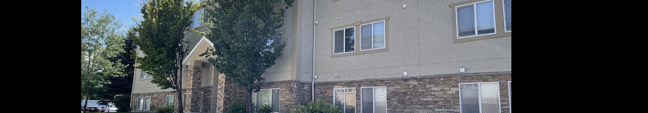 Charming apartment building with stone accents, lush greenery, and sunny skies, offering a welcoming and tranquil environment.
