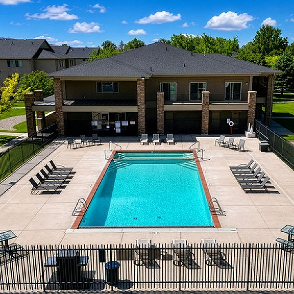 Inviting outdoor pool area at an elegant apartment complex, surrounded by sun loungers and lush greenery, perfect for relaxation and leisure.