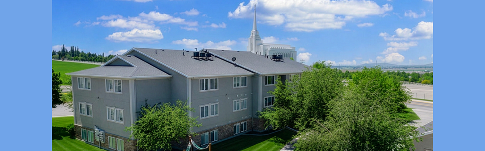 Charming apartment building nestled amidst lush greenery with a scenic view and a beautiful spire in the background, perfect for serene living.