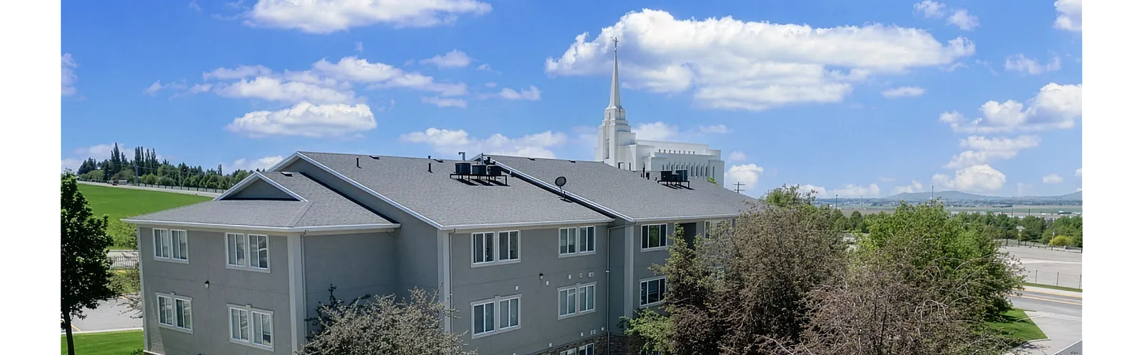 Charming apartment building surrounded by lush greenery and clear blue skies, featuring spacious yards and mature trees for serene living.