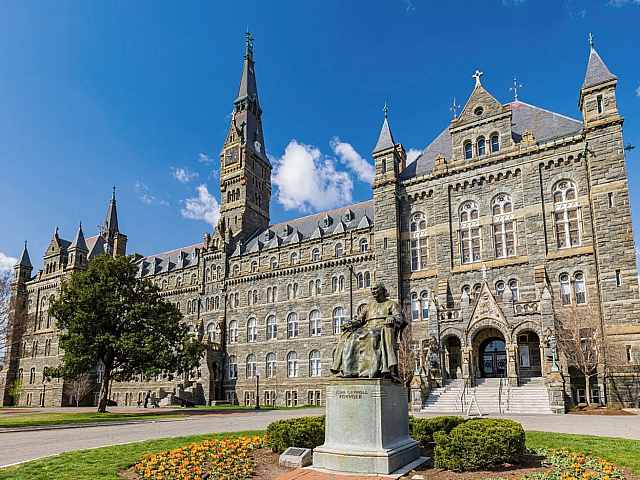 Majestic historic building with Gothic architecture, featuring a towering spire and detailed stonework under a bright blue sky.
