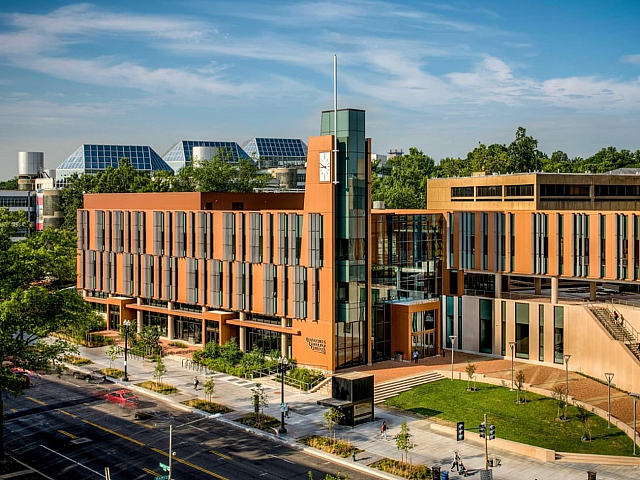 Modern architectural building with large windows and surrounding greenery under a clear blue sky.