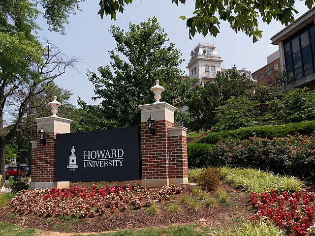 Elegant entrance of Howard University featuring a brick signpost with lush greenery and vibrant flowers, under a clear blue sky.