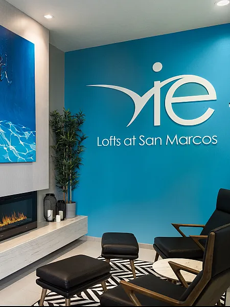Chic and modern lobby at Lofts at San Marcos featuring stylish seating, elegant decor, and a cozy electric fireplace against a vibrant blue accent wall.