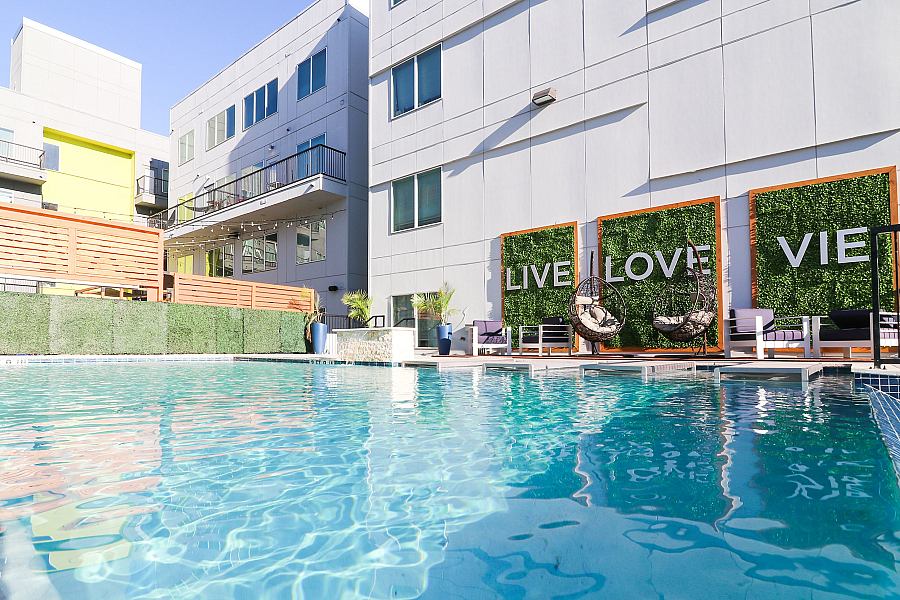 Modern apartment complex with a luxurious pool, stylish hanging chairs, and vibrant greenery, creating an inviting outdoor lounge area.