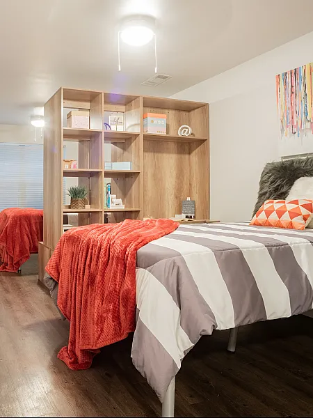 Contemporary bedroom with sleek wooden flooring, twin beds adorned with vibrant red throws, and a stylish open shelf divider.