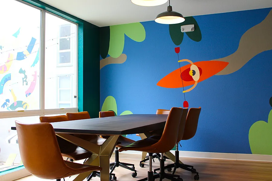 Bright and modern meeting room featuring a vibrant wall mural with a kayak design and stylish leather chairs around a sleek table.