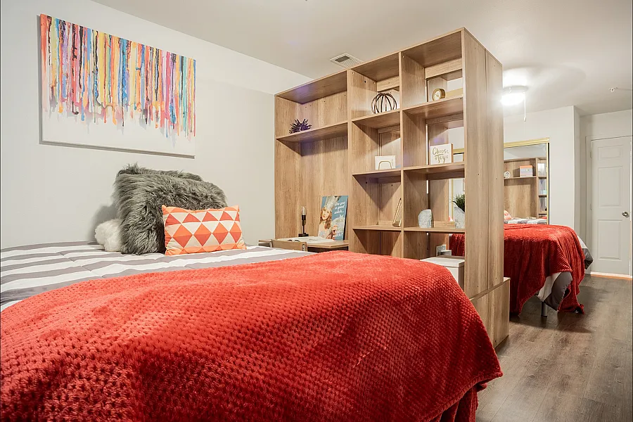 Chic bedroom with vibrant red coverlet, cozy pillows, and modern wooden shelving for a stylish and functional living space.