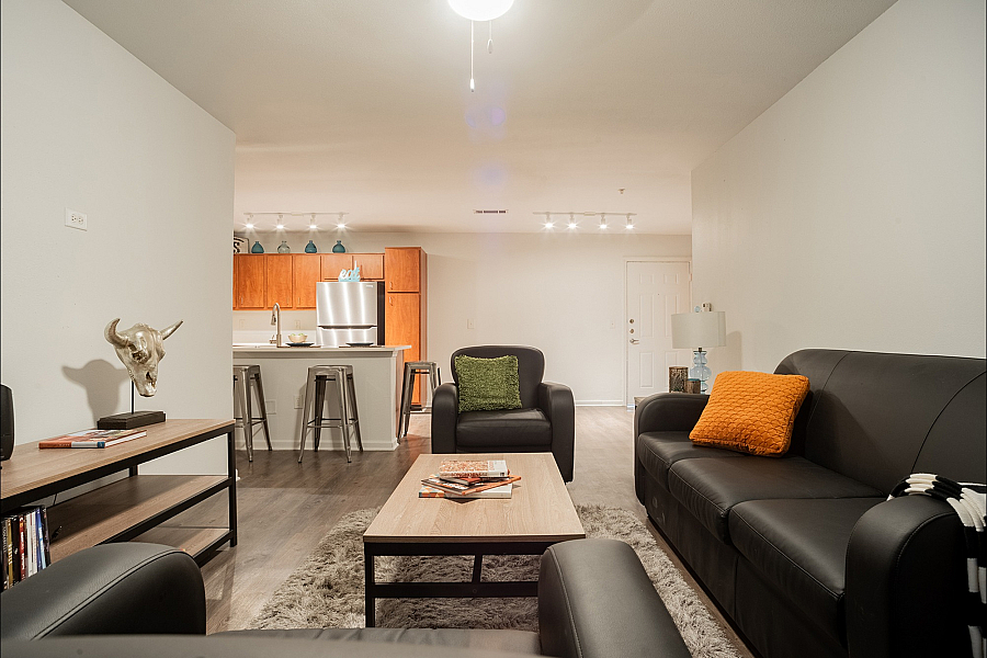 Inviting living room with sleek black leather sofas, vibrant cushions, and a cozy atmosphere, seamlessly flowing into a modern kitchen with stainless steel appliances and stylish bar seating.