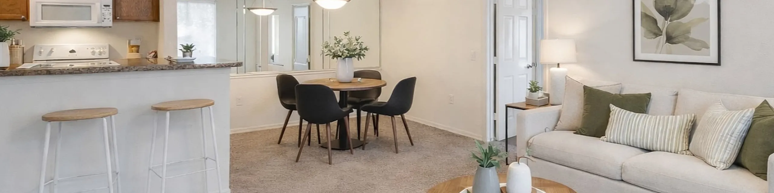 Open concept living and dining space. beige sofa with green accent pillows. wood and black coffee table. wood dining table with black chairs.