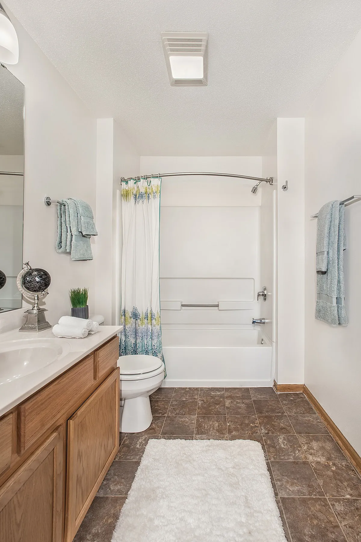 Bright and modern bathroom featuring elegant tile flooring, a sleek vanity, and a stylish shower area with vibrant floral curtain.
