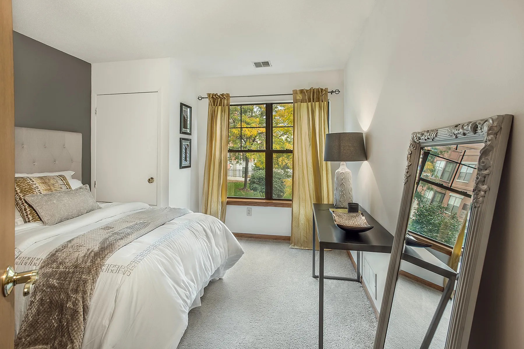 Cozy bedroom with stylish decor, featuring a plush bed, large window with lush views, elegant mirror, and chic lighting.