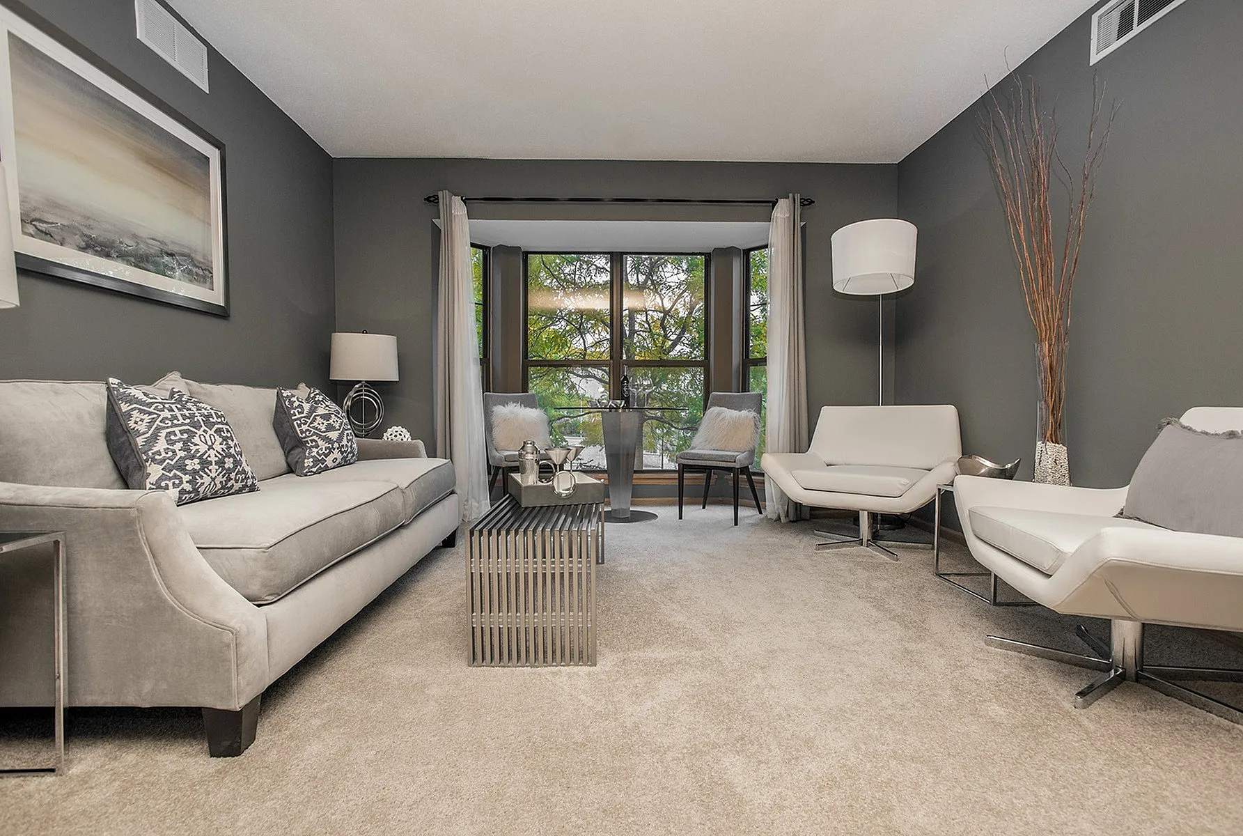 Elegant living room with plush gray sofa, modern chairs, and large windows offering scenic views, ideal for relaxation and entertainment.
