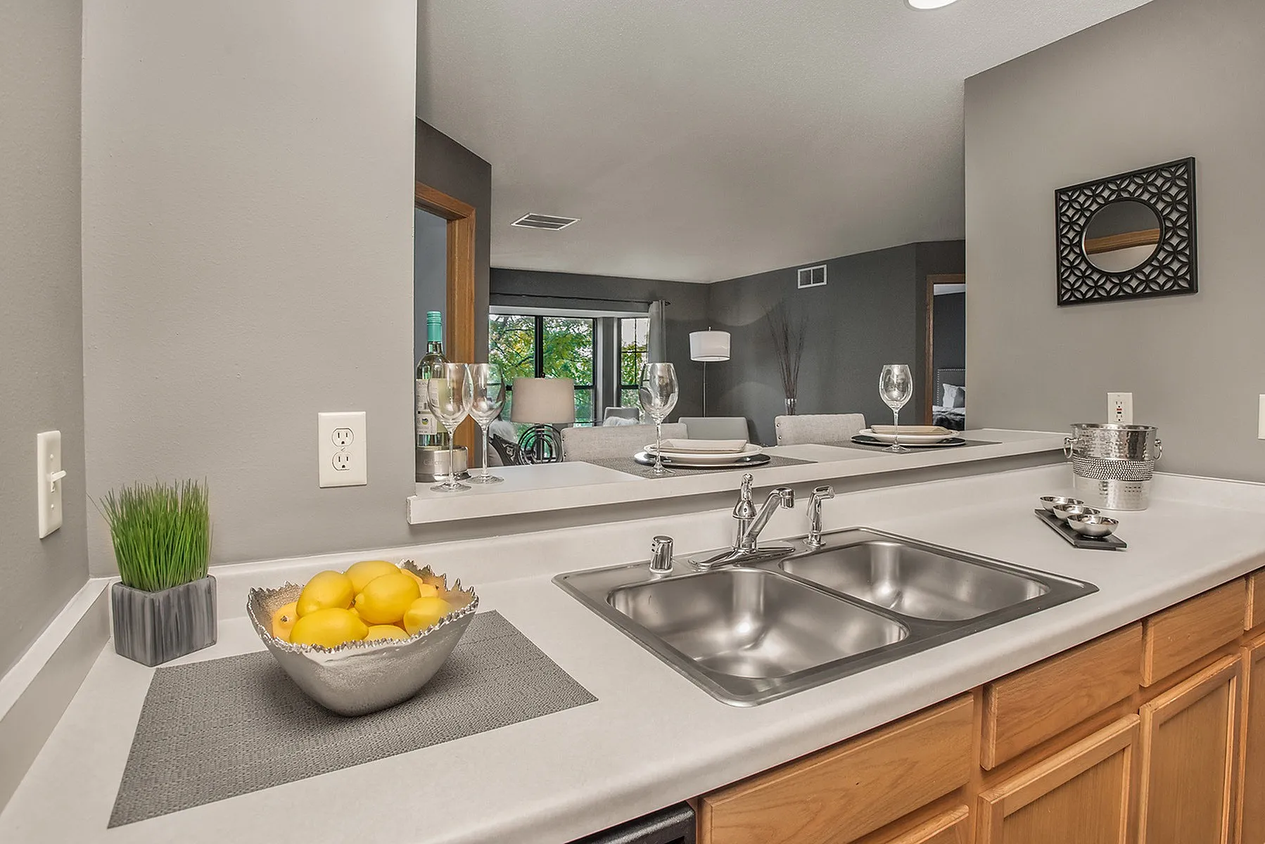 Modern apartment kitchen with sleek countertops, stainless steel sink, and open view into a cozy living room, warmly lit and inviting.