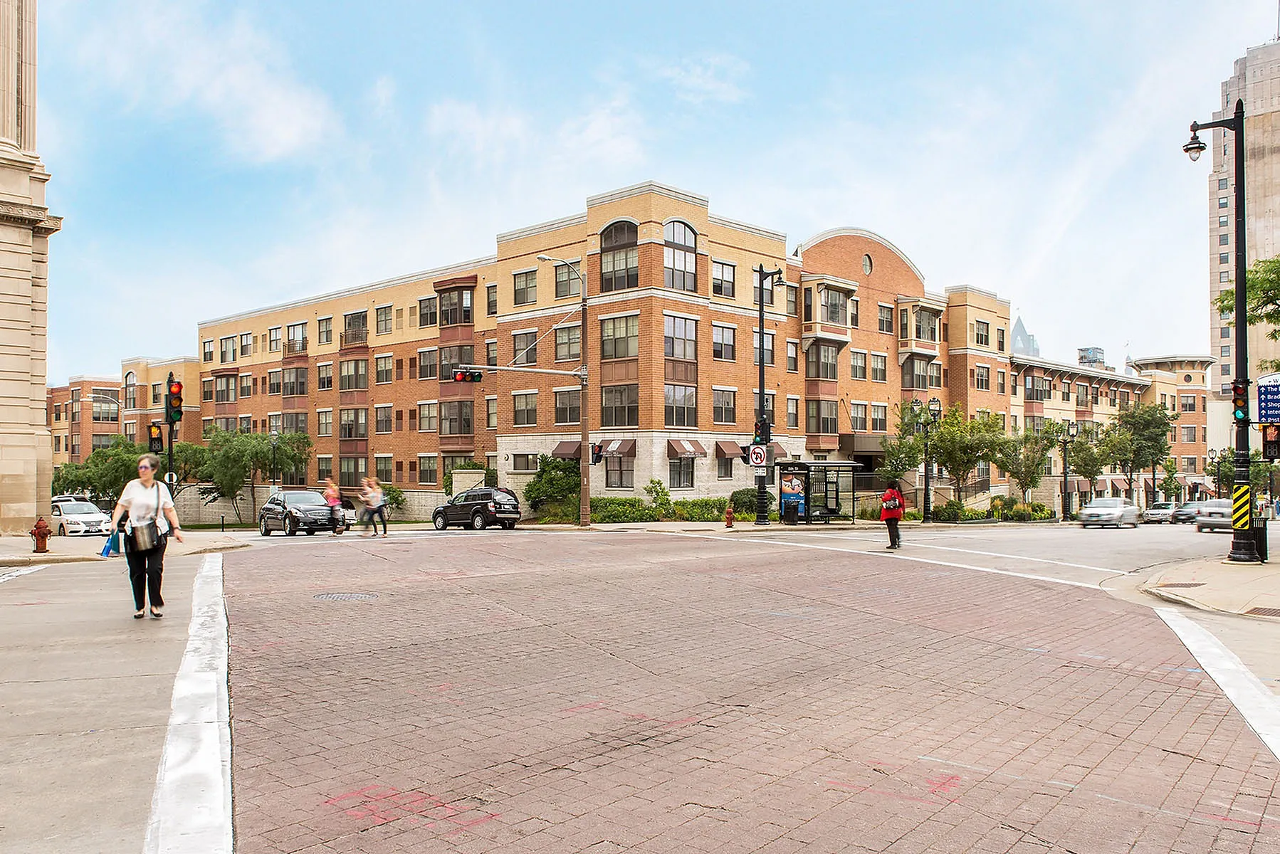 Charming urban apartment complex with modern architectural design, highlighted by red brickwork and large windows, situated on a bustling city corner.