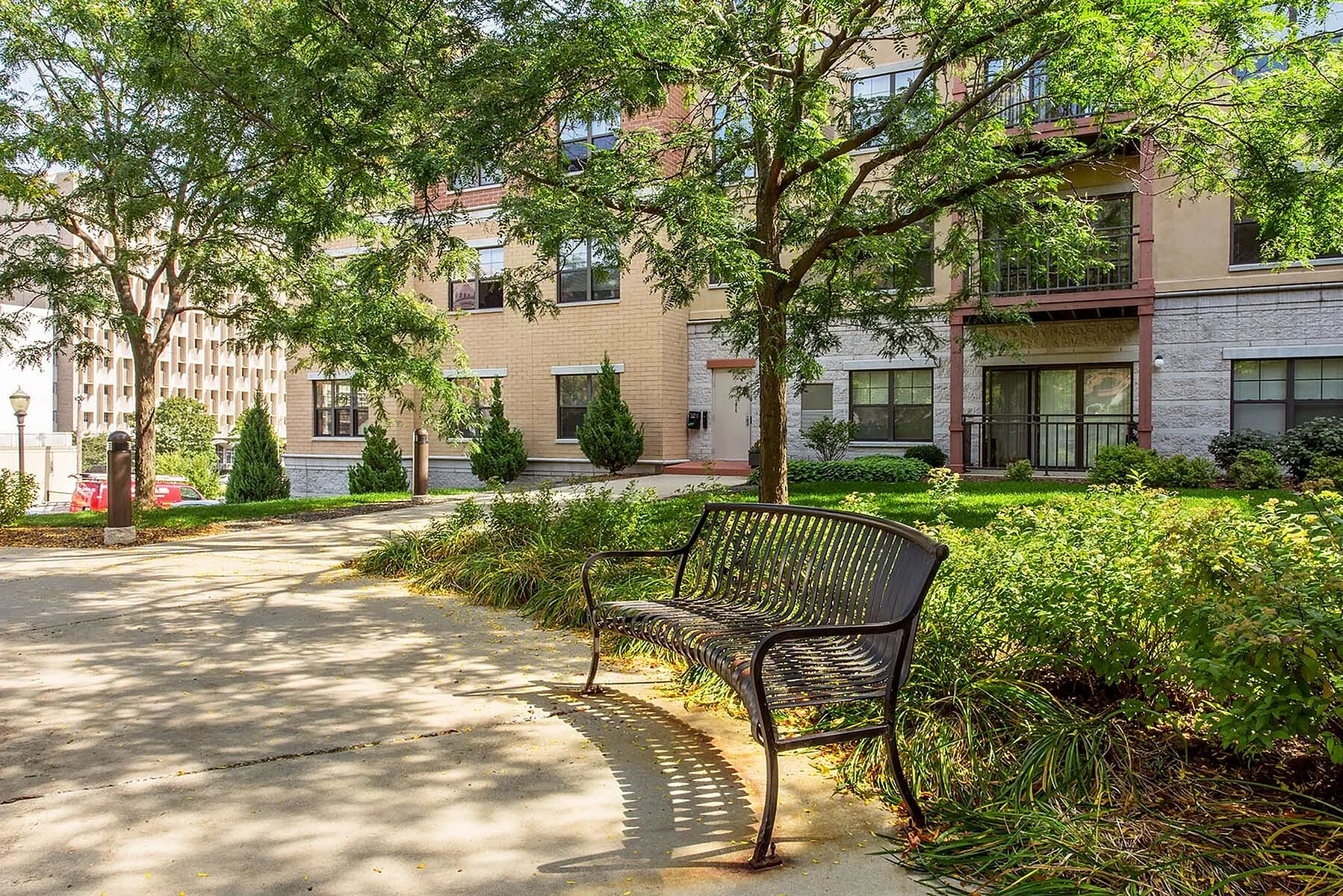 Charming apartment building façade surrounded by lush greenery and a peaceful garden bench.