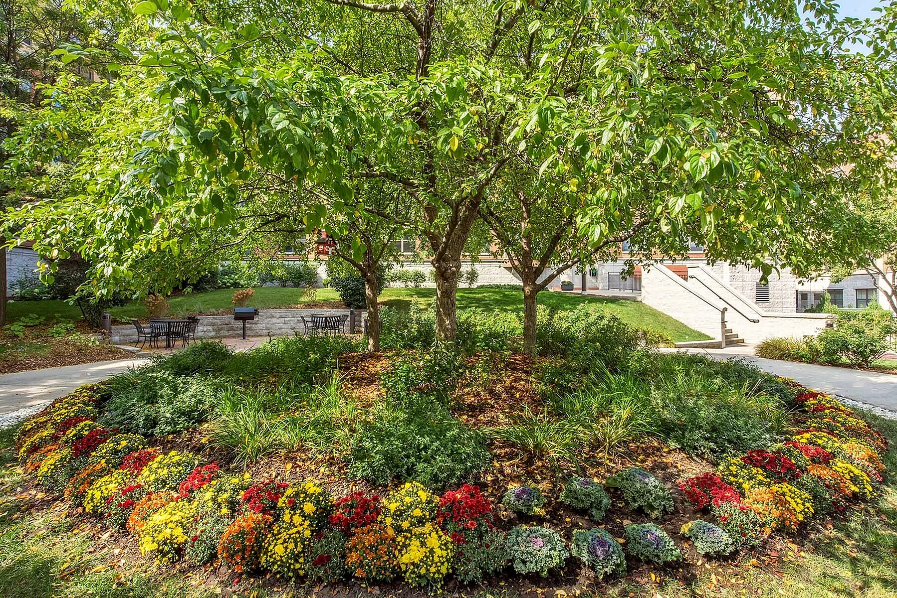 Charming garden with lush green trees, vibrant blooming flowers, and a peaceful seating area, ideal for relaxation.