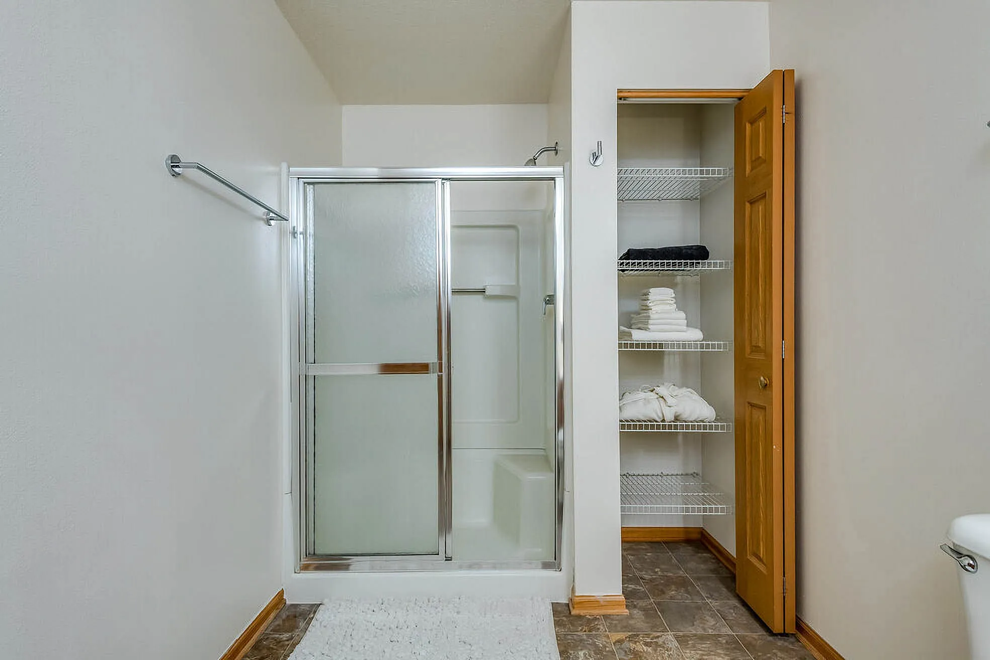 Modern bathroom with sleek glass shower, spacious linen closet, and elegant tile flooring.