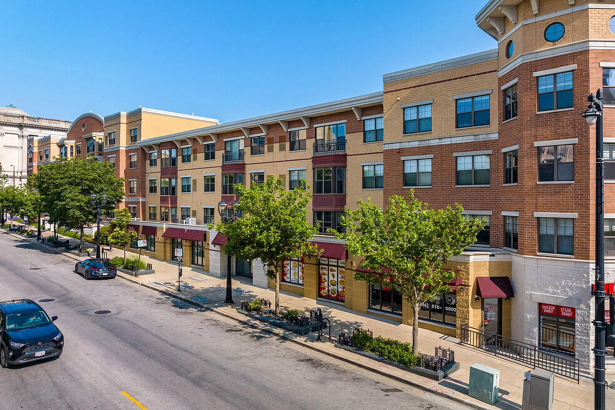Modern urban apartment complex with stylish brick facade, lush greenery, and convenient street-level retail spaces.
