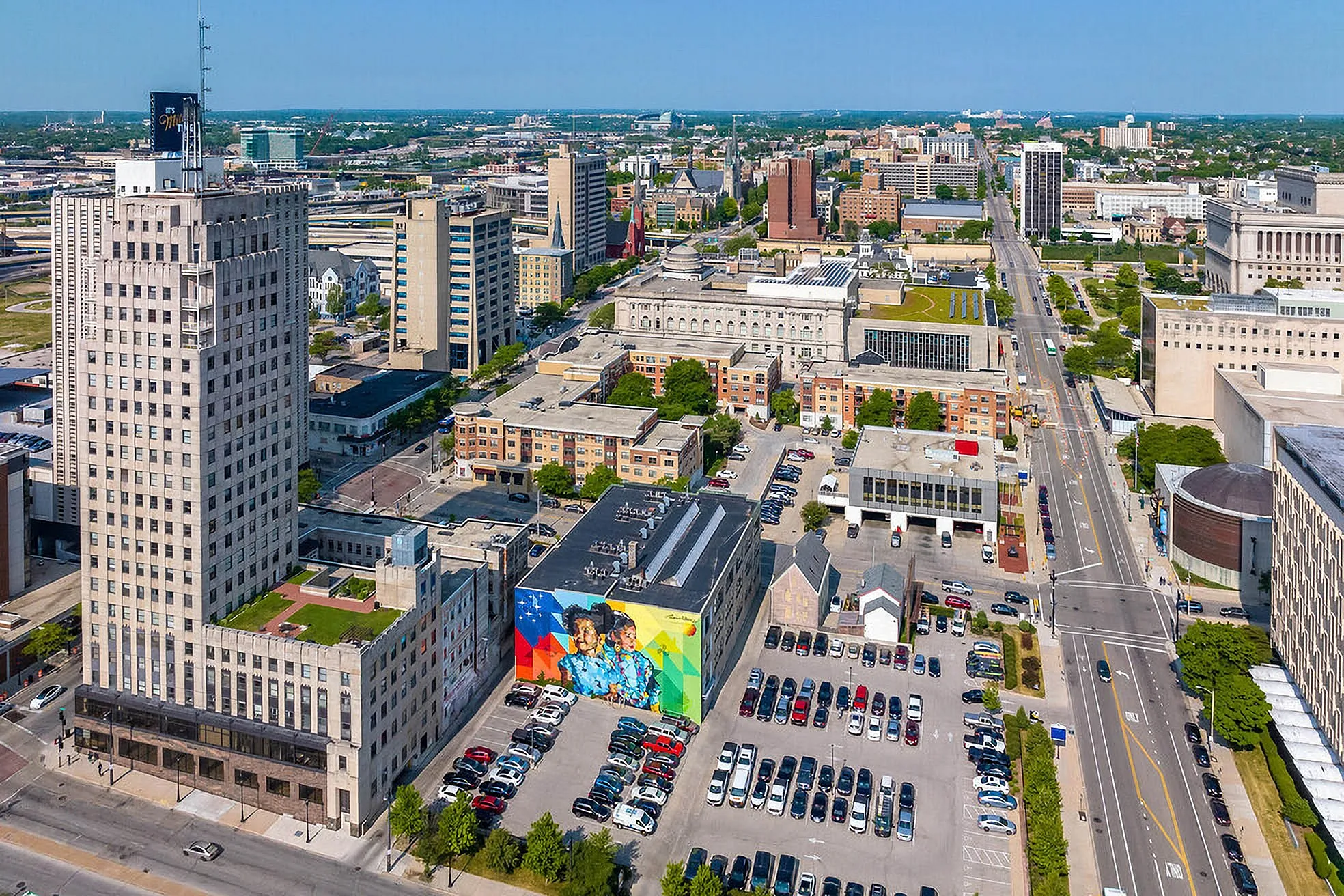 Vibrant cityscape showcasing a mix of modern and historic architecture, colorful mural, and urban green spaces under a clear blue sky.