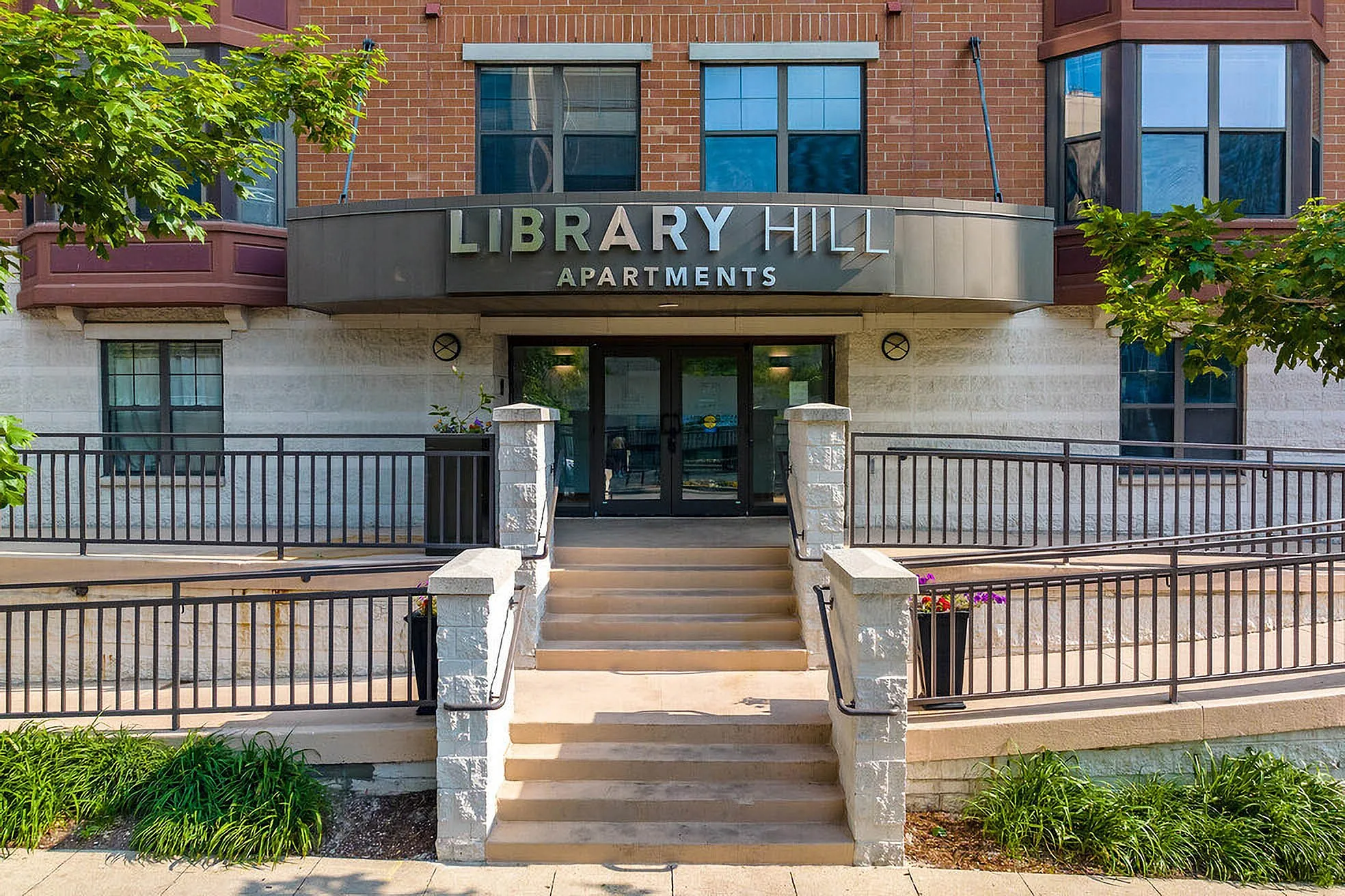 Inviting entrance to Library Hill Apartments with landscaped greenery and modern architecture.