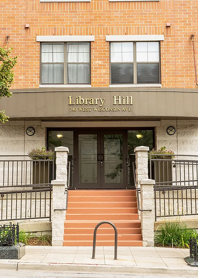 Charming brick apartment building entrance at Library Hill, showcasing a welcoming front staircase and lush greenery.