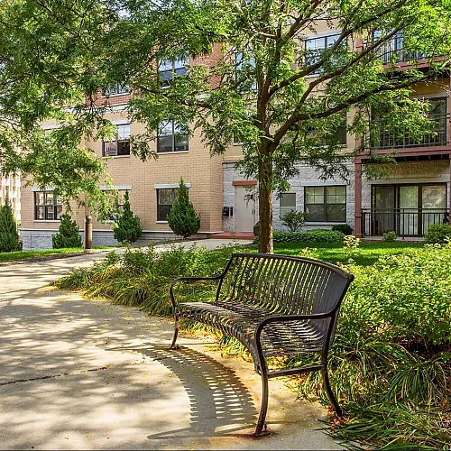 Charming apartment exterior with lush greenery, a peaceful pathway, and a welcoming bench.