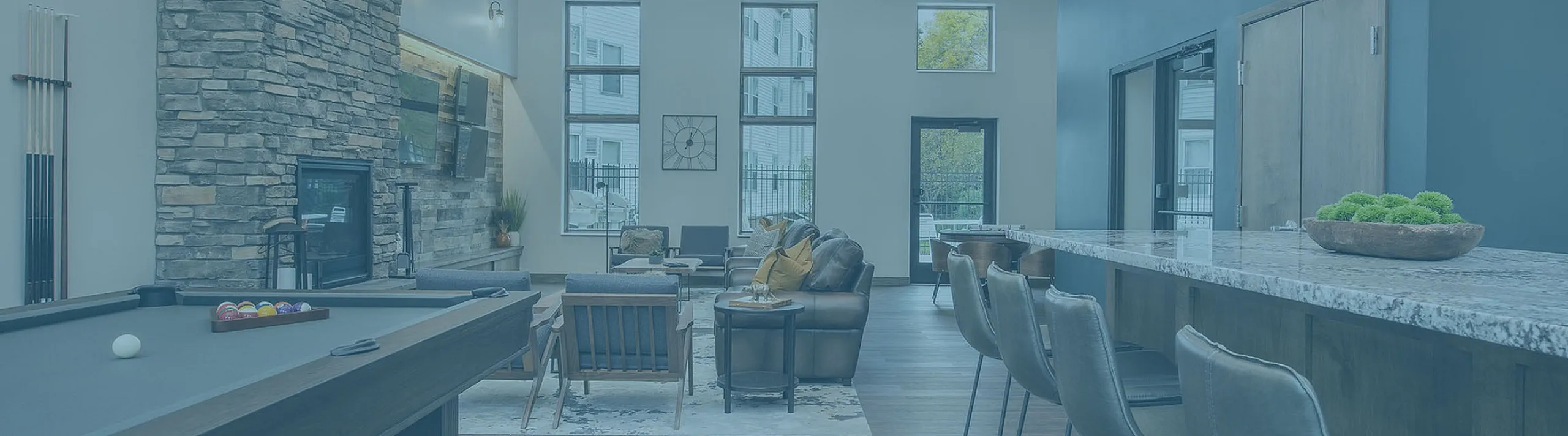 Modern apartment lounge showcasing a cozy seating area, rustic stone fireplace, and a sleek pool table, ideal for entertainment and relaxation.