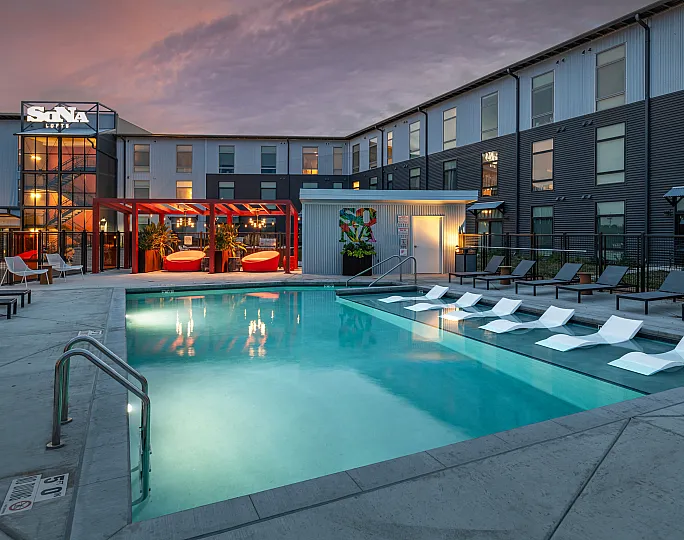 Luxurious apartment complex with a stunning outdoor pool, cozy lounge chairs, and vibrant evening ambiance.