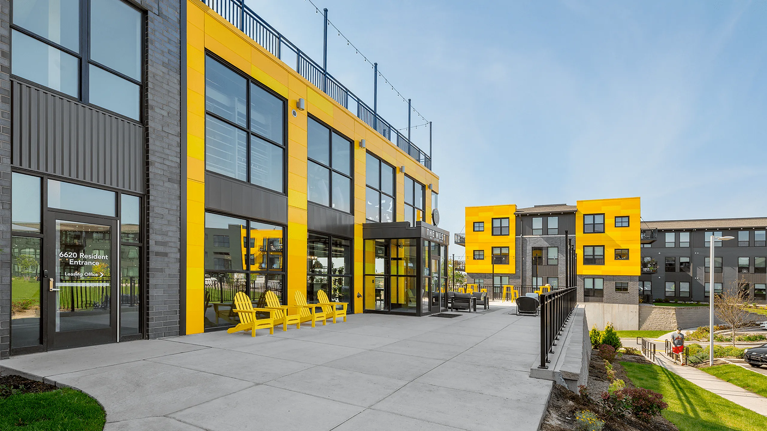 Modern apartment complex exterior with vibrant yellow accents, abundant windows, and inviting outdoor seating area.