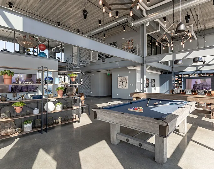 Chic loft-style common area featuring modern industrial design with a pool table, stylish decor, and loft railing overlooking a cozy lounge.
