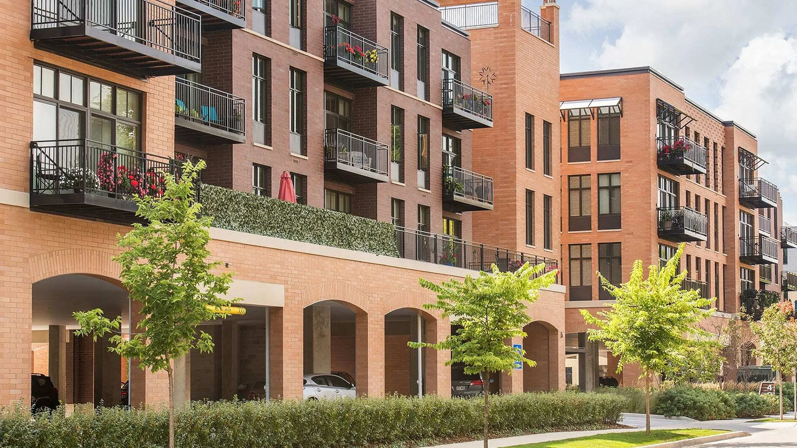 Charming modern apartment complex with brick facade, private balconies, and lush greenery, offering urban living with a touch of nature.