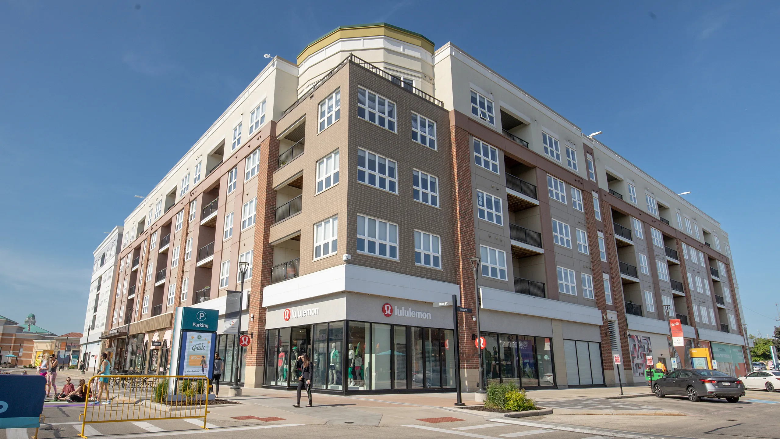Modern multi-story building with retail space on the ground floor, featuring large windows and balconies, set against a clear blue sky.