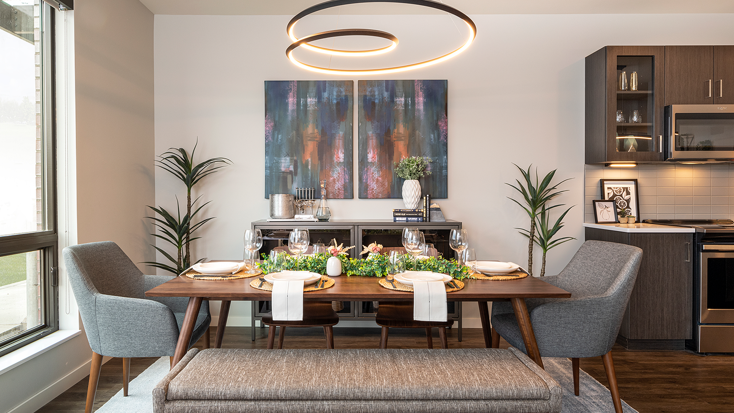 Elegant dining area with modern decor, wooden table set for four, stylish pendant light, and contemporary artwork.