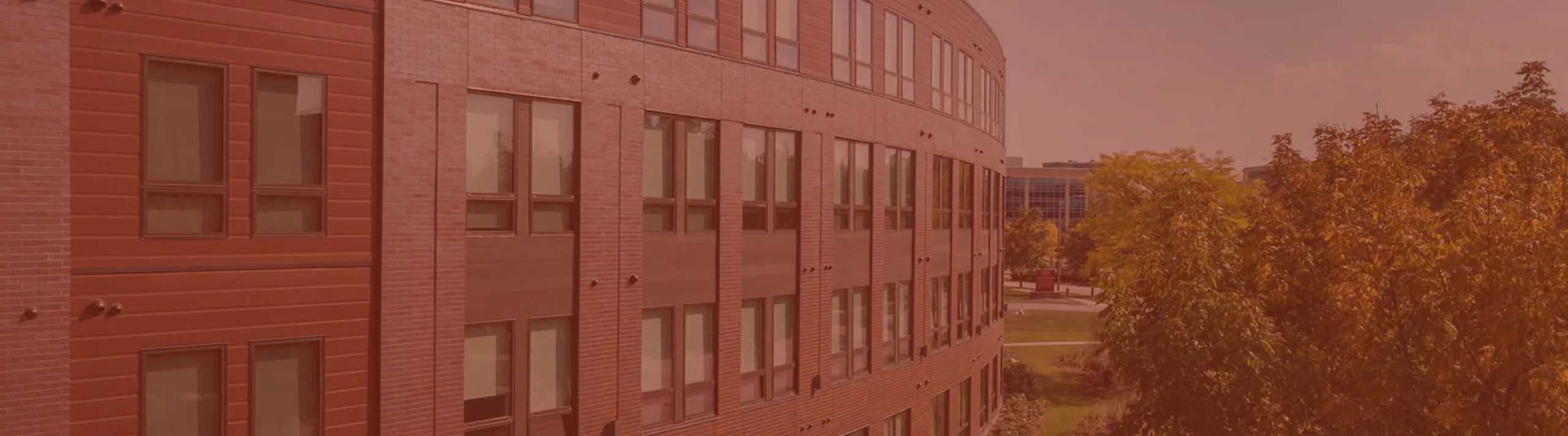 Modern apartment building with sleek red brick facade, surrounded by lush greenery and clear blue sky.